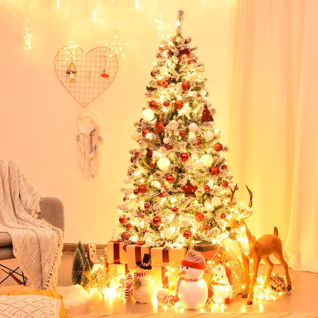 Costway 6ft Pre-Lit Premium Snow Flocked Hinged Artificial Christmas Tree with 250 warm white LED lights, featuring 600 branch tips with a snow-kissed appearance. The tree is displayed in a cozy indoor setting, decorated with red and white ornaments, surrounded by festive decor including gift boxes, a snowman, and a reindeer. The sturdy metal stand ensures stability, and the hinged design allows for easy assembly and storage.