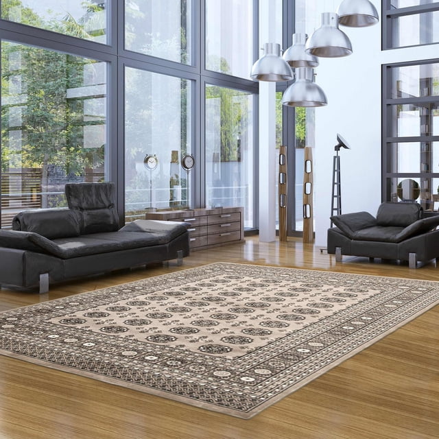 Tekke Oriental Area Rug for Living Room, Dining Room, Bedroom in grey with symmetrical oval motifs and a detailed border, placed on polished wood flooring between two black leather sofas in a modern living room with large windows and metallic pendant lights. This traditional Oriental rug features a soft pile and elegant pattern, suitable for enhancing living, dining, or bedroom areas.