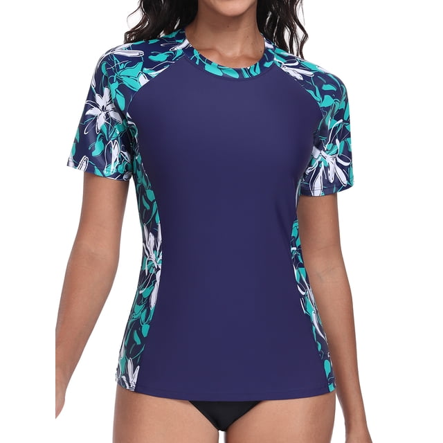 Charmo Color Blocked Swimsuit Tops for Womens Sun Protection UPF 50+ Rash Guard Quick Dry Running Swim Shirts. This short-sleeve rash guard features a navy blue body with plant-based printed sleeves in teal and white floral patterns. Made from 82% nylon and 18% spandex, it offers UPF 50+ sun protection, quick-dry fabric, and a 4-way stretch for flexibility. Suitable for swimming, surfing, running, and other outdoor activities.
