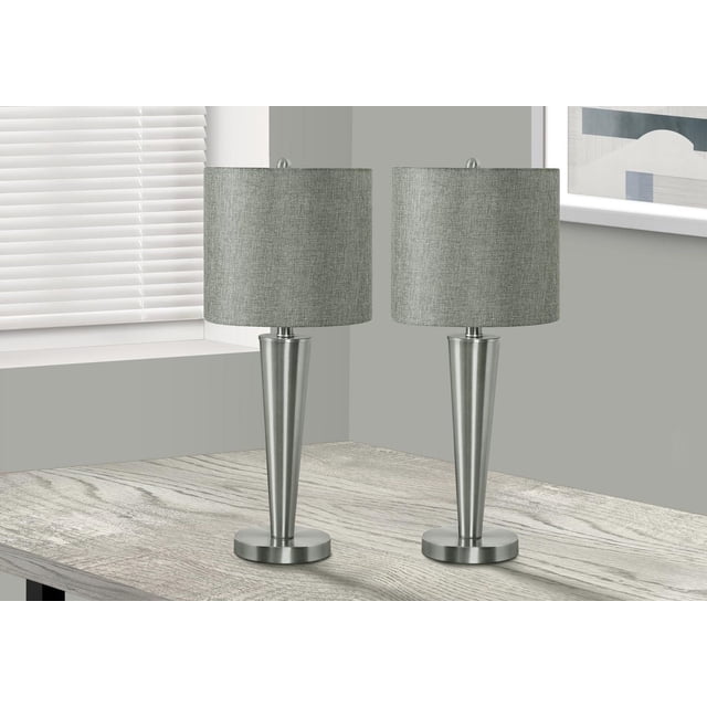 Monarch Specialties Lighting set of 2 contemporary 24-inch table lamps with tapered nickel metal bases, round metal bottoms, grey linen drum shades, and round metal finials, each featuring a rotary switch and USB port, displayed on a light wood table near a window with blinds and grey walls with framed artwork.