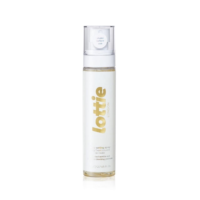 Lottie London - Dewy Setting Spray with Niacinamide and Blue Light Blocking Platinum (80ml) in a clear cylindrical bottle with white and gold lettering, featuring a white spray pump and transparent cap, designed to set makeup with a hydrating glass skin finish and micro-pearls for subtle radiance.