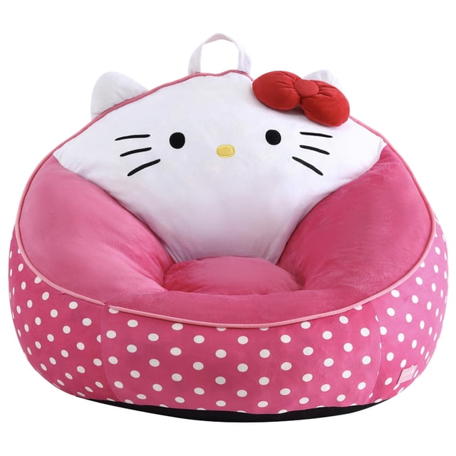 Hello Kitty Kids' Compressed Foam Bean Bag Chair in pink with white polka dots, featuring a micromink plush shell shaped as Hello Kitty's face with embroidered black eyes, whiskers, yellow nose, and a red bow on the upper right, designed for children with a built-in carrying handle for easy transport.