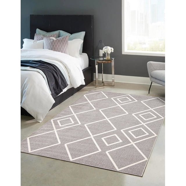 ECARPET washable geometric area rug and runner in grey with white square and diamond pattern, low pile polyester texture, placed on a concrete floor in a modern bedroom with a black upholstered bed, white bedding, and a glass side table with flowers near a large window, ideal for living rooms and high traffic areas.