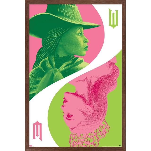 Wicked - Reflection Wall Poster with Push Pins, 22.375" x 34" features two stylized female profiles in green and pink tones divided by a white curved line. The upper green profile wears a wide-brimmed hat and cloak on a pink background, while the lower pink profile with a crown faces upward on a green background. The poster is framed in dark wood and includes gothic-style letters in matching colors on opposite corners, ideal for bedroom or office wall decor.