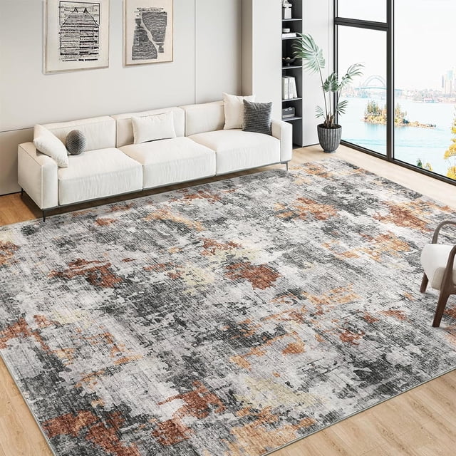 Twister.CK Washable Abstract Area Rug, 6' x 9', displayed in a stylish living room with a white sofa and large windows. The rug features a low pile design with a gray base and abstract patterns in rust, beige, and cream tones. Its washable and non-slip backing makes it ideal for high-traffic areas, pet-friendly homes, and modern spaces.