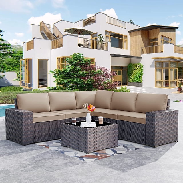 Kullavik Ensemble de Mobilier de Patio 6 Pcs avec Canapé Sectionnel d'Extérieur Toutes Saisons, construction en Rotin Osier Tressé à la Main, Coussins de Couleur Sable et table à Dessus en Verre Trempé. Cet Ensemble Modulaire de conversation pour Patio Est Disposé en Forme de L sur un Patio en Béton, avec une Maison Moderne et une Verdure Luxuriante en Arrière-Plan.