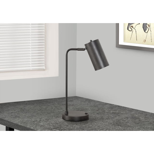 Monarch Specialties Lighting 18-inch modern table lamp with a cylindrical grey metal adjustable shade and round base, featuring a rocker switch and built-in USB port on the base, placed on a dark grey textured desk near a window with white blinds and framed artwork on the wall.