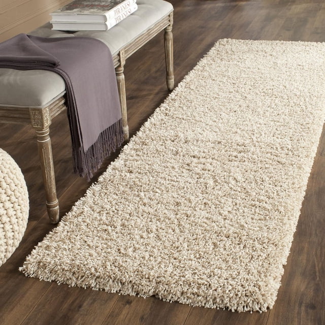 Safavieh California Tapis Shag en Peluche Uni beige avec un Empilage de Polypropylène dense de 4,5 Kg/m2, Exposé sur un Plancher de Bois Franc Foncé à Côté d'Un Banc en Bois avec un Coussin Gris et un Jeté Gris Foncé, Convient pour Ajouter une Douceur Pelucheuse et un style Décontracté de la Côte Ouest aux Zones d'Accent dans les Maisons Canadiennes.