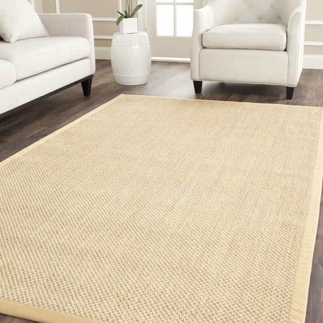 Safavieh Natural Fiber Juniper Border Area Rug with woven sisal texture in light beige and solid border, placed on dark hardwood floor between cream sofa and armchair in a bright living room with white ceramic planter, ideal for coastal or casual décor.