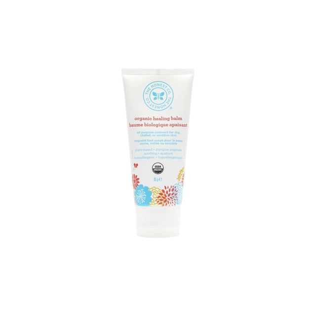 The Honest Company Organic Healing Balm in an 85g white squeeze tube with blue, red, and yellow floral designs, a plant-based salve for dry, chafed, or sensitive skin, suitable for baby skin care and moisturizing.