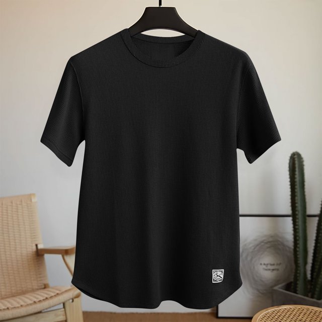 Men's solid color comfortable sport casual short-sleeved round neck shirt in black, made of 95% polyester and 5% spandex for a breathable and lightweight feel. The shirt features a ribbed texture, short sleeves, and a round neckline, ideal for spring and summer activities such as fitness exercises or casual daily wear. Displayed on a hanger in a minimalist indoor setting with a chair and cactus in the background.