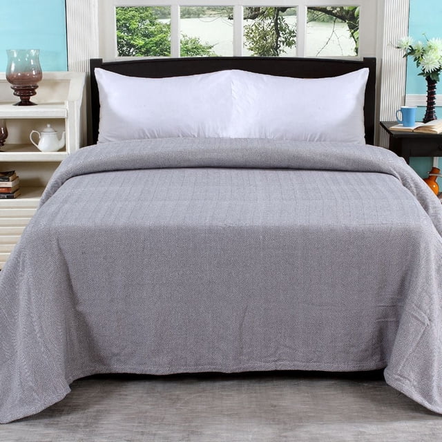 Fabstyles 100% Cotton Soft and Cozy Blanket in grey and white herringbone weave covering a queen (90''x90'') bed with white pillows in a bright bedroom with window views of greenery and bedside tables holding a glass lamp, teapot, and flowers, suitable for layering and all-season comfort.