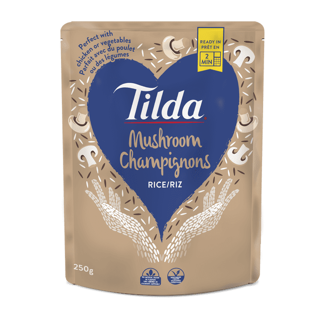 TILDA Sachet de Riz aux Champignons avec Fond beige et Grand Cœur Bleu Affichant la Marque et le Nom du Produit Riz aux Champignons. l'Emballage de 250 g Est Prêt en 2 minutes au Micro-Ondes, Idéal pour Accompagner le Poulet Ou les Légumes, Ne Contient Pas de Colorants Ni d'Arômes Artificiels, et Est Végétarien et Végane.