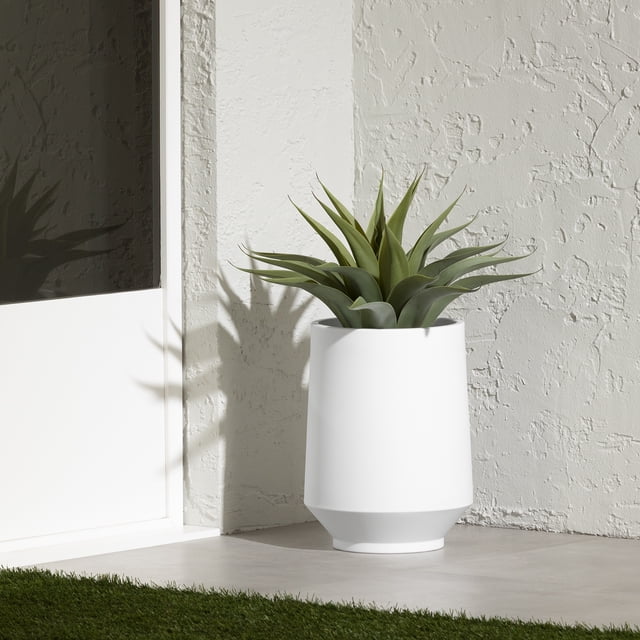 South Shore Dalya Jardinière Blanche, Jardinière de Jardin en Polyéthylène Résistant aux Intempéries avec une Forme Cylindrique Effilée, Posée sur un Plancher de patio Gris contre un Mur Blanc Texturé Près d'Une Porte Blanche, Tenant une Plante Succulente Verte avec des Feuilles Pointues, Convient à une Utilisation Intérieure Ou Extérieure Toute l'Année.