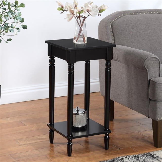 French Country Table d'Appoint Kim avec Tablette en Fini Bois Noir par Convenience Concepts, Idéale comme Table de Chevet Ou Table d'Appoint. Comprend des Pieds Tournés Sculptés et Deux Niveaux d'Étagères pour Rangement Ou Exposition. Fabriquée en Bois Massif et Manufacturé avec une Finition Noire Lisse Sans Plomb. Dimensions : 14 Po L x 14 Po L x 28 Po H. Exposée dans un Salon à Côté d'Un Fauteuil Gris avec accents Décoratifs sur les Étagères.