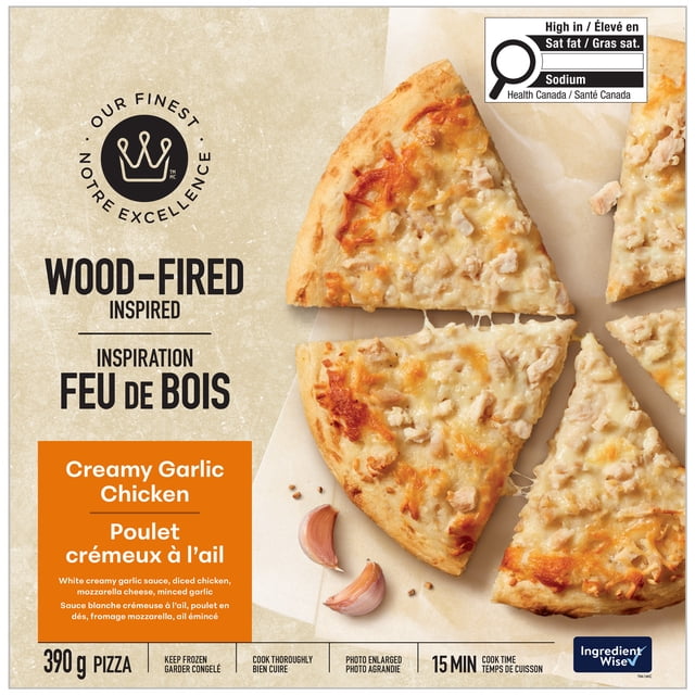 Our Finest Wood-Fired Inspired Creamy Garlic Chicken Pizza with four slices topped with white creamy garlic sauce, diced chicken, and melted mozzarella cheese on a crispy golden crust with light smoky char, displayed on parchment paper with garlic cloves, ready in 15 minutes from frozen.