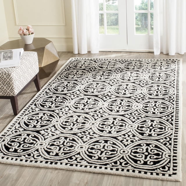 SAFAVIEH Cambridge Leslie Geometric Area Rug in black and white hand-tufted wool with repeating circular geometric patterns and textured high/low pile, placed on light hardwood floor near white curtains and a patterned bench, ideal for modern home or office decor.