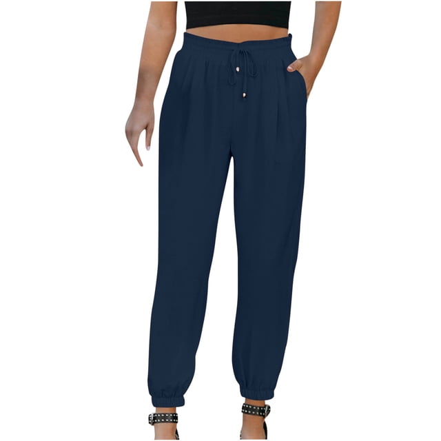 Jovati Woman Solid Color Cotton and Linen Drawstring Elastic Waist Long Straight Pants in a navy blue shade. These ankle-length pants feature a casual style with an elastic waistband, drawstring closure, and side pockets. Made from lightweight cotton and linen fabric, they are designed for comfort and versatility, suitable for casual, daily, or vacation wear. The model is shown wearing the pants with a black cropped top and studded sandals.