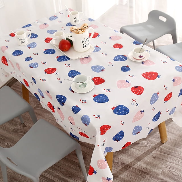 Zanvin Tablecloths, waterproof and oil-proof tablecloth for kitchen and dining table. The tablecloth features a vibrant strawberry-themed print in red, blue, and pink on a white background. It is made of PVC material, measuring 90cm x 137cm, and includes decorative fringe edges. Suitable for various uses such as dining tables, outdoor patio tables, and kitchen tables. The tablecloth is lightweight, heat-insulating, non-slip, and easy to clean with machine wash. Displayed on a wooden dining table with grey chairs and tableware.