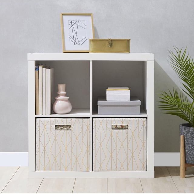 Hometrends Organiseur à 4 cubes en Fini grain de Bois Blanc avec Quatre Compartiments de 13 Pouces L x 15 Pouces P x 13 Pouces H. le Dessus Contient une Impression Abstraite Encadrée et une Boîte en Métal Dorée. des cubes Supérieurs Exposent des Livres, un vase Rose et des Boîtes de Rangement Empilées. les cubes Inférieurs Contiennent Deux Bacs en Tissu beige avec des Lignes Géométriques Dorées. Positionné sur un Plancher de Bois Clair contre un Mur Gris à Côté d'Une Plante Verte en Pot, Idéal pour le Rangement au Bureau Ou au Salon.