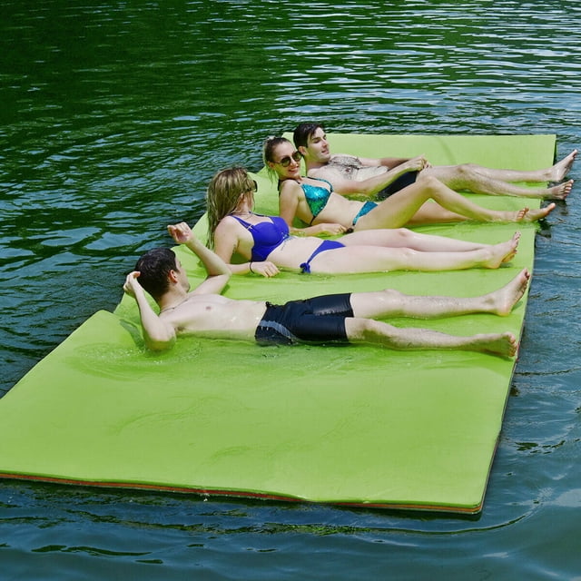 Gymax 12' x 6' Floating Water Pad Mat in green, made of 3-layer tear-resistant XPE foam, shown in use on a lake with multiple people lounging on its surface. The mat measures 12 feet long, 6 feet wide, and 1.5 inches thick, offering a durable and buoyant platform for relaxation or water activities. Lightweight and easy to roll up for storage, it includes straps and a bungee tether for secure anchoring. Suitable for pools, lakes, and beaches.