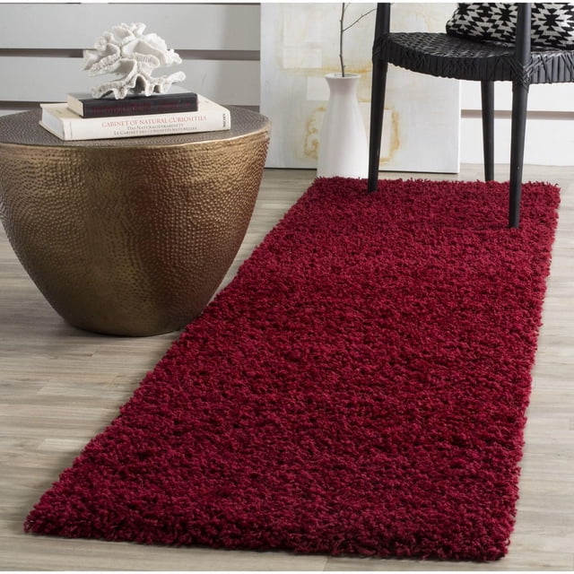 Safavieh Athens Tapis Shag en Peluche Uni Rouge Foncé, Montré comme un Coureur Rectangulaire sur Plancher de Bois Clair à Côté d'Une table d'Appoint en bronze Martelé avec des Livres et une Déco Corail, et une Chaise Tissée Noire avec des Coussins à Motifs, avec un Doux Poil en Polypropylène Idéal pour les Intérieurs Transitionnels et Convient pour Ajouter de la Chaleur aux Espaces Étroits.