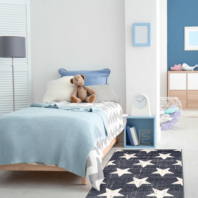 ECARPET Kids Room, Nursery, Playroom, Bedroom Area Rug, Angel Collection with a dark rectangular rug featuring large white stars, crafted from ultra soft yarn for durability and softness, placed beside a child's bed with blue bedding and teddy bear in a bright kids' bedroom with light wood flooring and blue accents, ideal for high traffic and pet-friendly areas.