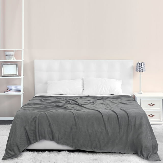PiccoCasa Cooling Blanket Viscose from Bamboo Breathable Dark Gray Full size displayed on a neatly made bed with a white tufted headboard. The lightweight blanket, made from 100% viscose derived from bamboo, features a soft, breathable texture and a dark gray color. The setting includes a minimalist bedroom with a white nightstand, a lamp, and a light beige wall.