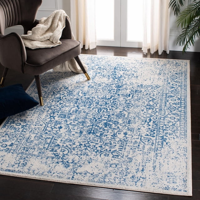 Safavieh Evoke Trena Tapis Traditionnel pour Aire en Bleu et Crème à Motif floral Usé en Frise de Polypropylène Douce, Posé sur un Plancher de Bois Franc Foncé à Côté d'Un Fauteuil Brun Foncé avec des Pattes à Embout Doré et un Jeté beige, Rideaux Blancs Quasi Transparents et une Plante Verte, Convient à la Déco Décontractée du Salon.