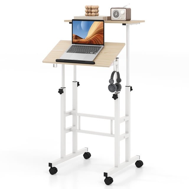 Giantex Mobile Standing Desk in natural finish, featuring a height-adjustable sit-to-stand design with a two-tier structure. The upper desk panel is set higher for additional storage or display, while the lower panel includes a tilting surface with an edge stopper, ideal for reading or typing. The desk is supported by a sturdy white metal frame with four universal casters, two of which are lockable for stability. Includes two removable hooks for accessories like headphones. Compact and portable, suitable for home office or study use.