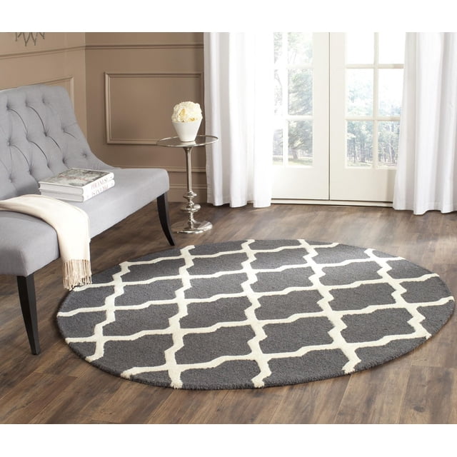 Safavieh Cambridge Liam Tapis Géométrique pour Aire, Rond avec Velours de Laine Gris Foncé et Motif de Treillis Géométrique Blanc Cassé, sur Plancher de Bois Franc dans une Pièce Lumineuse avec un Banc Capitonné Gris, table d'Appoint Chromée avec des Fleurs Blanches, et Rideaux Blancs au-Dessus de Portes en Verre, Idéal pour Ajouter un style et une texture Américains Modernes à la Maison Ou au Bureau.