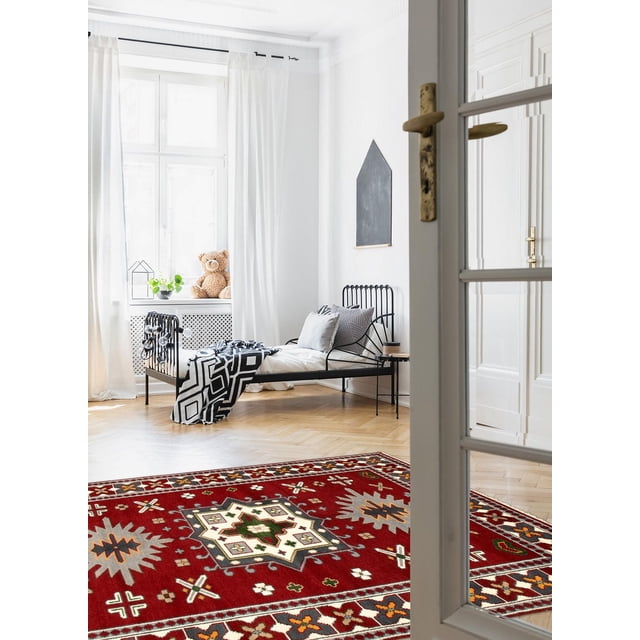 ECARPETGALLERY 100% Wool Traditional Indoor Area Rug with bold geometric Persian Kazak-inspired patterns in red, cream, green, and orange tones, placed on light hardwood flooring in a bright bedroom featuring a black metal bed frame with white and gray pillows, a black and white geometric throw, and a window with white curtains and a teddy bear on the sill, suitable for entrance, bedroom, living, or dining rooms.