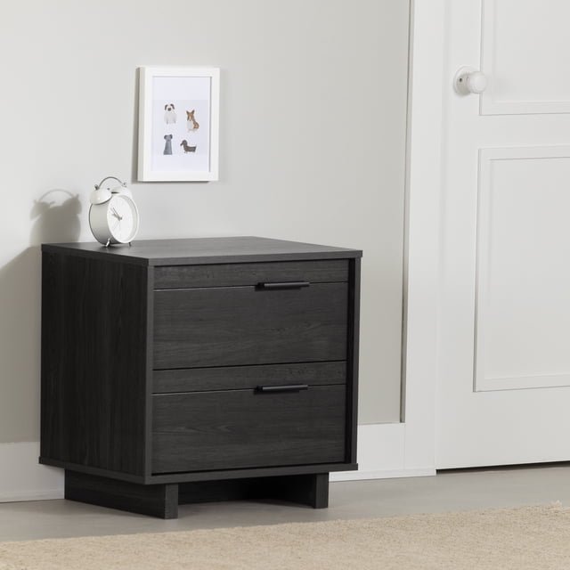 South Shore Fynn 2-Drawer Nightstand in gray oak with two spacious drawers featuring sleek black metal handles and smooth metal slides, standing on a low base on a light floor against a pale wall with a white framed dog print and a white alarm clock on top, suitable for kids' rooms storage.