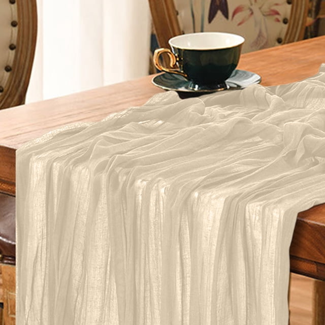 Dvruxg Cheesecloth Table Runner in a rustic gauze design, displayed on a wooden table with a teacup in the background. The long table runner measures 35 x 70 inches, offering a soft and textured look suitable for weddings, birthday parties, and other special events. Its neutral tone complements various decor styles, and it is machine washable for easy maintenance.