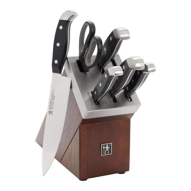 HENCKELS Statement 7 Piece Self Sharpening Block Set, Brown front-facing view of a stained ash wood block with brushed stainless-steel top and labelled self-sharpening ceramic honing slots; five knives with matte black triple-rivet handles (3"/7.6 cm, 5"/12.7 cm, 6"/15.2 cm, 7"/17.8 cm, 8"/20.3 cm) plus kitchen shears, block dimensions 39.4 cm (15.5") x 11.1 cm (4.4") x 29.8 cm (11.7"); often used for trimming herbs with the shears.
