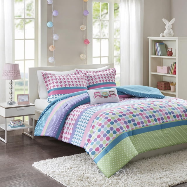 Home Essence Apartment Teen Linda Comforter Set on a bed featuring multi-colour oversized polka dots, stripes, houndstooth, and small polka dots patterns. Includes two standard shams with pink houndstooth and aqua stripes, plus a decorative pillow embroidered with three owls. The comforter reverses to aqua blue. The bedroom has white curtains, a pink lamp on a nightstand, and a white bookshelf with decor.