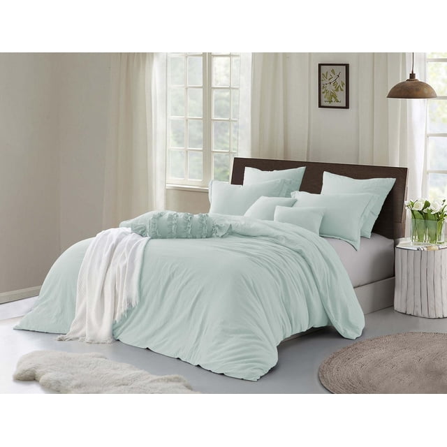 Natural Crinkle Fabric Ultra Soft Solid Duvet Cover Set in soft pastel blue with crinkled microfiber texture on a bed with dark wood headboard and matching pillow shams, styled with a white knitted throw and round woven rug in a bright bedroom with sheer curtains and rustic white side table with white flowers.