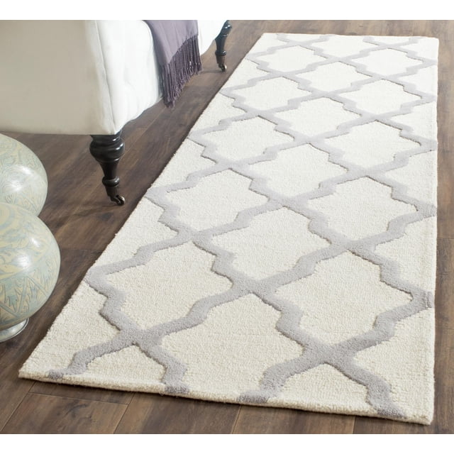 Safavieh Cambridge Liam Geometric Area Rug runner with white wool base and light gray geometric pattern, hand-tufted with plush cut and high/low loop piles, placed on dark hardwood floor beside white sofa leg and decorative ceramic spheres, ideal for home or office accent.