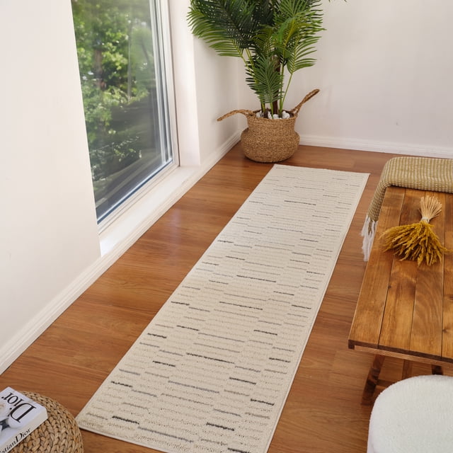 Rug Branch Nimbus Modern Indoor Area Rug, Cream Grey, Geometric - a long rectangular runner rug with a cream base and subtle grey geometric lines on a wooden floor by a large window. Ideal for high-traffic areas like kitchens and hallways, shown with a woven basket plant and wooden bench with a yellow throw and dried flowers.