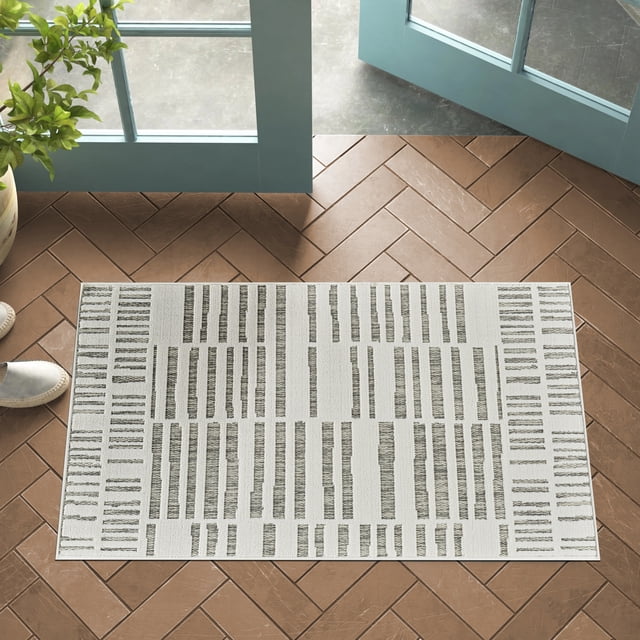 Rug Branch Maise Abstract Indoor Outdoor Area Rug in cream beige with a modern geometric pattern of vertical and horizontal lines, sized 2'7" x 4'11", placed on brown herringbone tile floor near open blue doors and a potted plant, suitable for entryway, hallway, kitchen, or bathroom use.