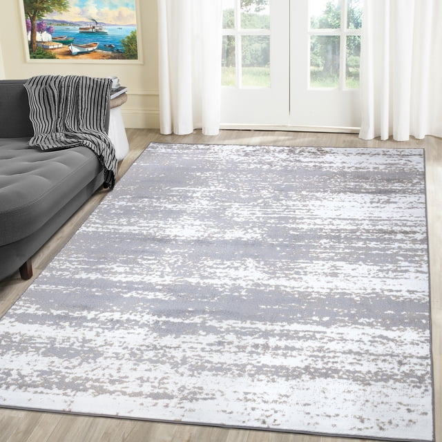 A2Z Palma 1787 Transitional Abstract Bedroom Small Area Rug Carpet Tapis displayed in a living room setting. The rug features a modern abstract design with a blend of light silver grey and white tones, creating a contemporary and vintage aesthetic. Made of 100% heat-set polypropylene with a medium pile thickness of 10mm, it offers a soft texture and durability. The rug is placed on a wooden floor near a grey sofa and large windows, adding a cozy and stylish touch to the space.