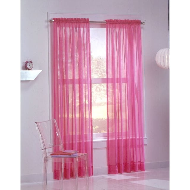 918 Calypso Voile Rod Pocket Curtains in pink sheer voile fabric with 5-inch bottom hems, machine washable, hanging on a silver rod over a window in a white room with a clear acrylic chair and a small shelf with a clock, suitable for light filtering and decorative window treatment.