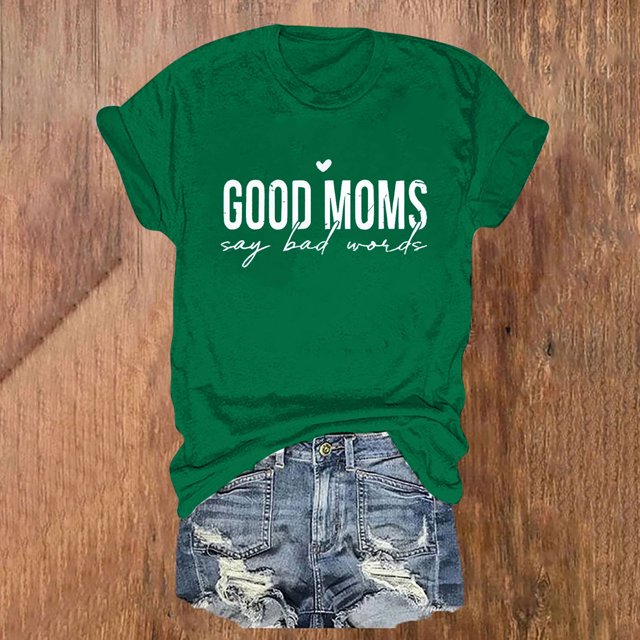 Pntutb T-Shirt à Col Rond Imprimé à Manches Courtes pour Femme, Chemise Décontractée Ample, Hauts en Vert avec un Texte Imprimé Blanc Qui Lit « les Bonnes Mamans Disent des Mots Mauvais ». le T-Shirt Présente une Encolure Ronde et des Manches Courtes, Style avec des shorts en denim Usés sur un Fond en Bois.