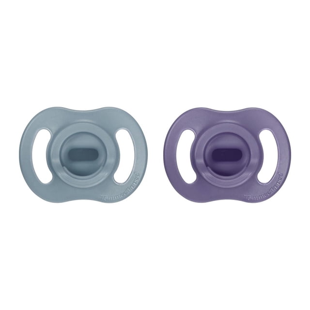 Tommee Tippee Ultra-light StayPut Pacifier 2 pack with one blue and one purple one-piece silicone pacifier featuring a symmetrical nipple and shield for a comfortable fit that stays put on baby's face, designed for airflow and easy sterilizing, shown on white background.