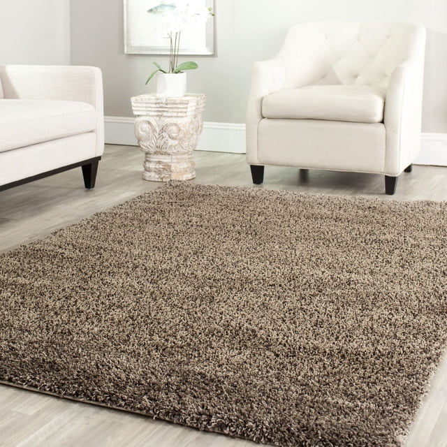 Safavieh California Tapis Shag en Peluche Uni Couleur taupe avec une pile de Polypropylène dense Pesant 4,5 kg par Mètre Carré, Placé sur un Plancher de Bois Clair entre un Fauteuil et un sofa Capitonnés Blancs, Présentant un Piédestal en Pierre Sculptée avec une Plante en Pot, Convient pour Ajouter Douceur et Chaleur aux Salons.