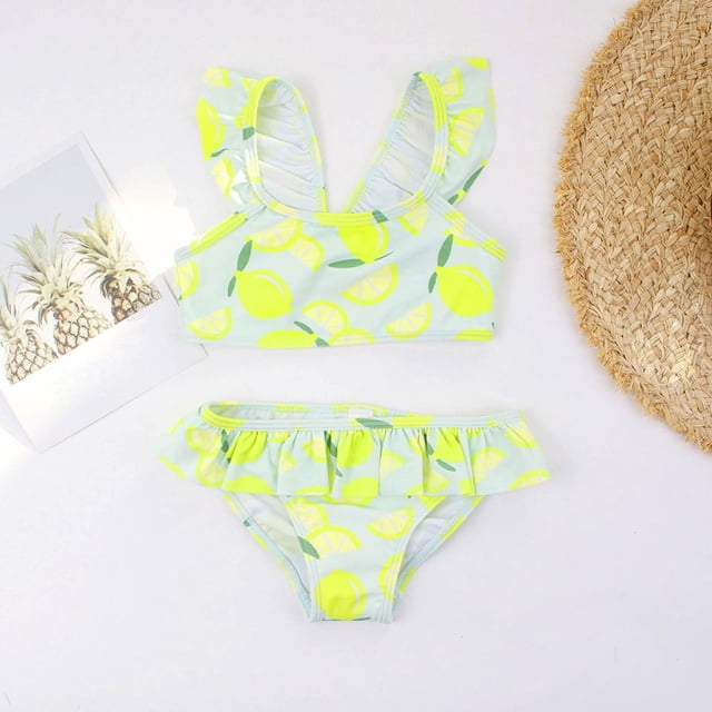 Kid Girls Swimsuits 2 Piece Beach Bikini Swimsuits Striped Ruffle Bathing Suit for Teens 5-6 Years. The swimsuit features a vibrant lemon print on a light blue background, with ruffled shoulder straps and a matching ruffled bikini bottom. Made from lightweight polyester, it is designed for comfort and quick drying. Suitable for beach outings, pool parties, and water activities. Shown alongside a straw hat and a pineapple-themed photo for a summery vibe.