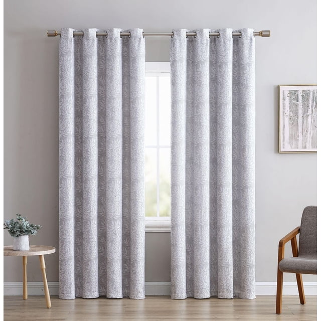 Jacquard Leaf Blackout Grommet Single Window Panel in grey with a textured leaf pattern and blackout lining, hanging from silver grommets on a metal rod. The 54-inch wide panel provides privacy and light blocking, suitable for living rooms, bedrooms, or offices. The setting includes a wooden floor, a small round table with a plant on the left, and a grey fabric chair with wooden arms on the right.