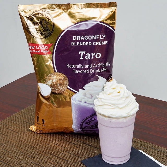 Big Train Mélange de Frappé Crème Mélangée Taro Libellule 3,5 lb, Boîte Blanche de 3,5 lb Orientée vers l'Avant avec Étiquette de Taro Violette et Marque a2zbaazar, Illustration d'Étiquette d'Un Frappé de Taro Violet et d'Une Cuillère en Bois de Mélange en Poudre sur Fond de studio Neutre, Indiquant une base de Frappé de Taro Crémeuse Sans Café et Sans Caféine, Convient aux Boissons dessert Mélangées.