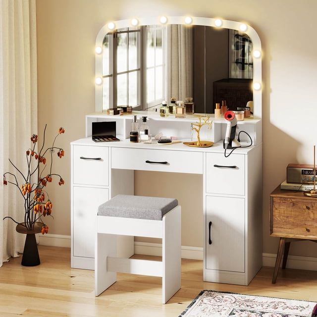 Costway Vanity Desk Makeup Table with Stool in white, featuring a large curved mirror with 10 dimmable LED bulbs offering 3 adjustable color temperatures. The desk includes a built-in charging station with AC outlets, USB, and Type-C ports, along with a cable management hole for a tidy setup. Ample storage is provided with open shelves, three drawers, and two enclosed cabinets. The set includes a padded stool for comfort and anti-toppling kits for safety. Displayed in a cozy bedroom setting with wooden flooring and decorative accents.