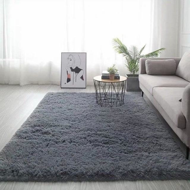 Cozival Shaggy Area Rug in grey, a microfiber shaggy floor mat measuring 60x90 cm. This non-slip, machine washable rug is ideal for bedrooms, living rooms, or dorms. Shown in a modern living room with a grey sofa, a round metal coffee table, and a potted plant, its soft, fuzzy texture enhances comfort and style.